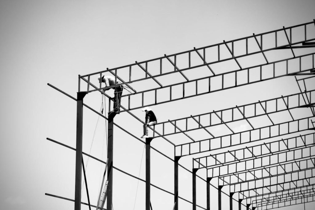 Black and white shot of construction workers atop a steel frame structure under a clear sky.